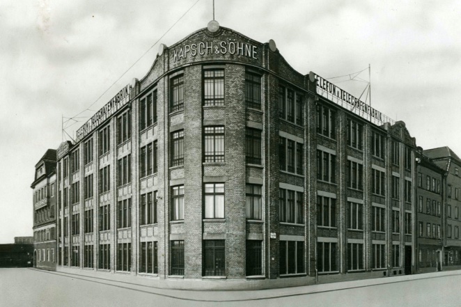 Schwarzweißfoto eines großen Gebäudes mit markanter Fassade und zahlreichen Fenstern, aufgenommen bei bewölktem Himmel.