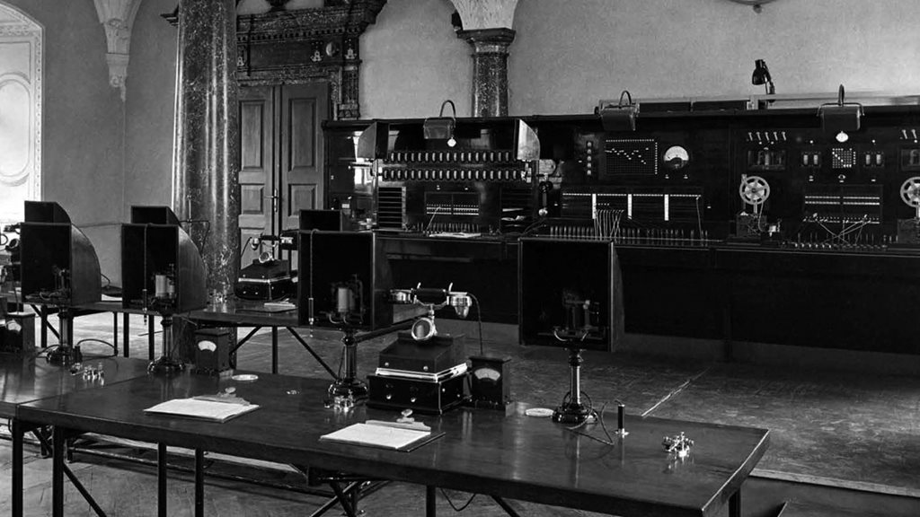 Ein großer Tisch in einem monochromen Raum mit mehreren Stühlen, passend zur Unternehmensgeschichte von Kapsch.