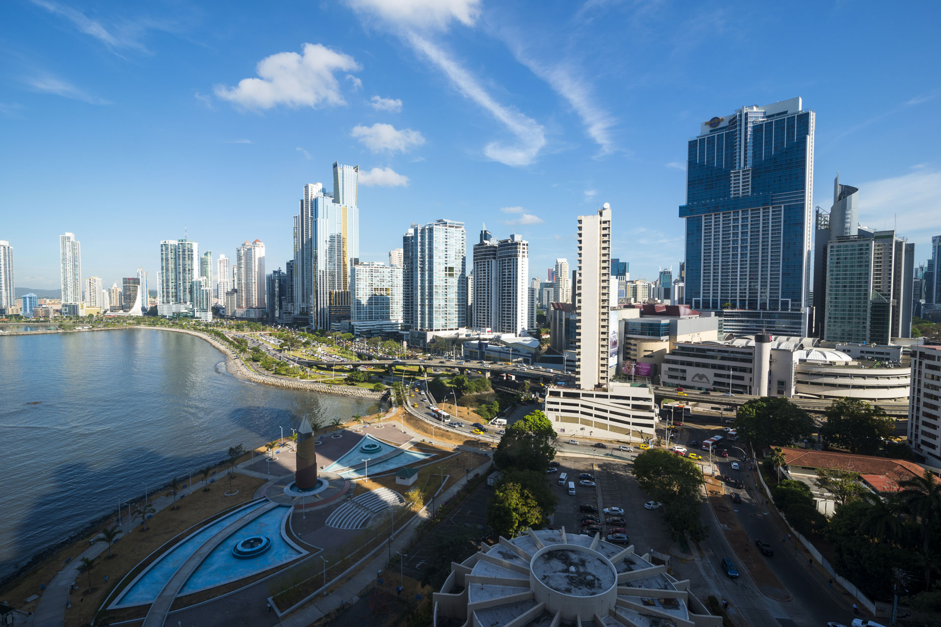 Stadtansicht mit Wasserfläche im Vordergrund, Wolken und Skyline im Hintergrund.