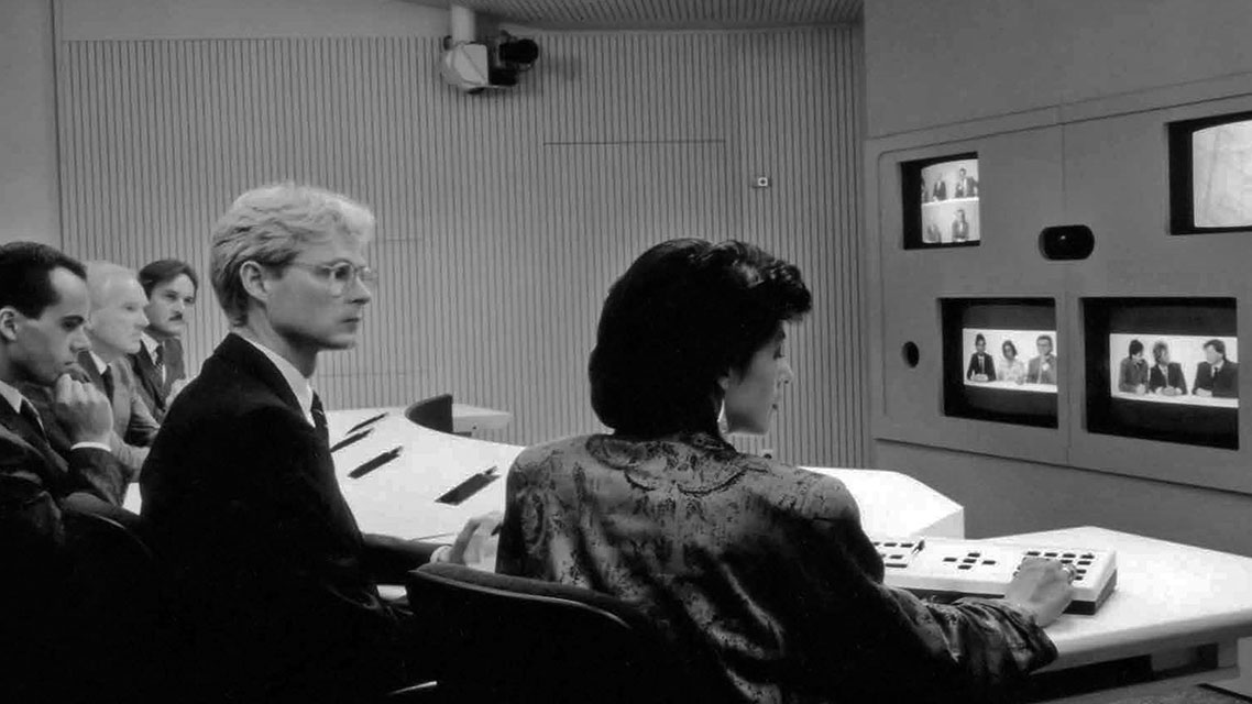 Ein Mann und eine Frau sitzen in einem Raum vor einem Fernseher, im Kontext der Unternehmensgeschichte von Kapsch.