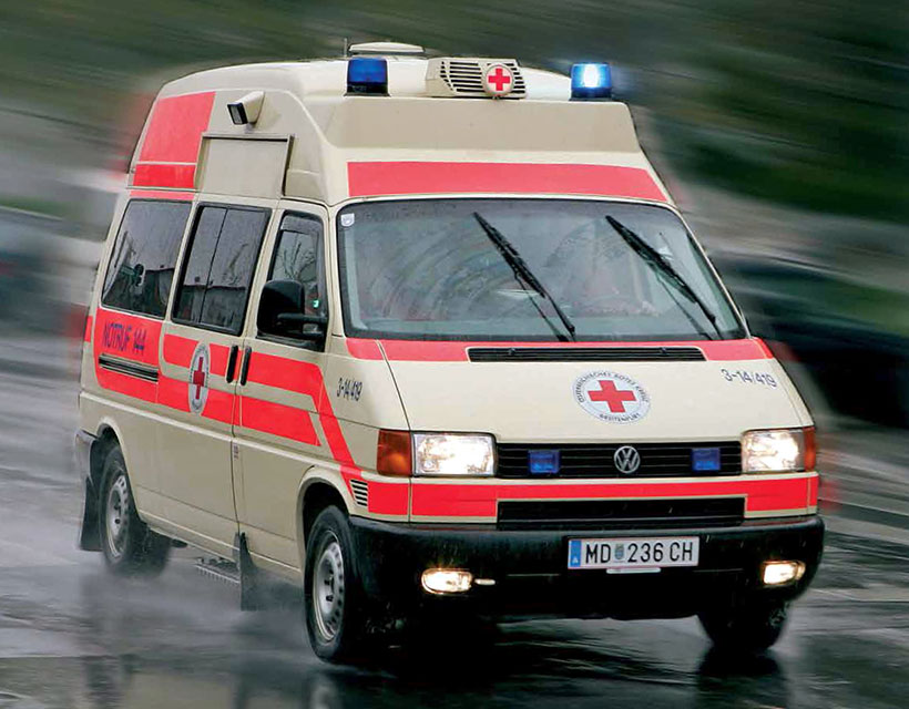 Eine rot-weiße Ambulanz auf einer nassen Straße.