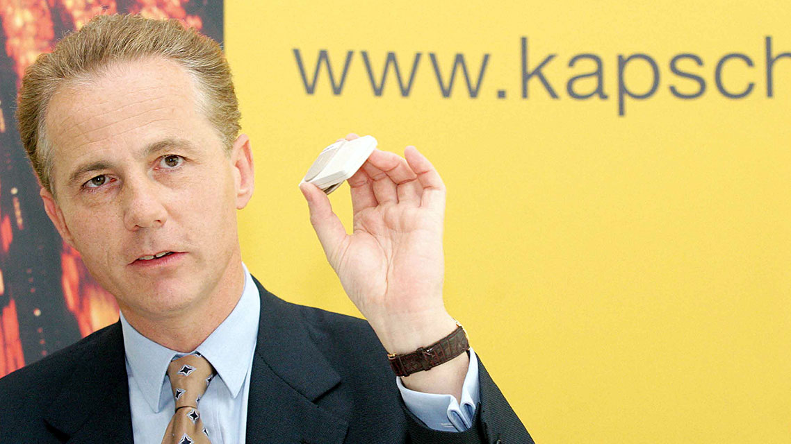 Ein Mann in Anzug hält ein kleines Objekt in der Hand.